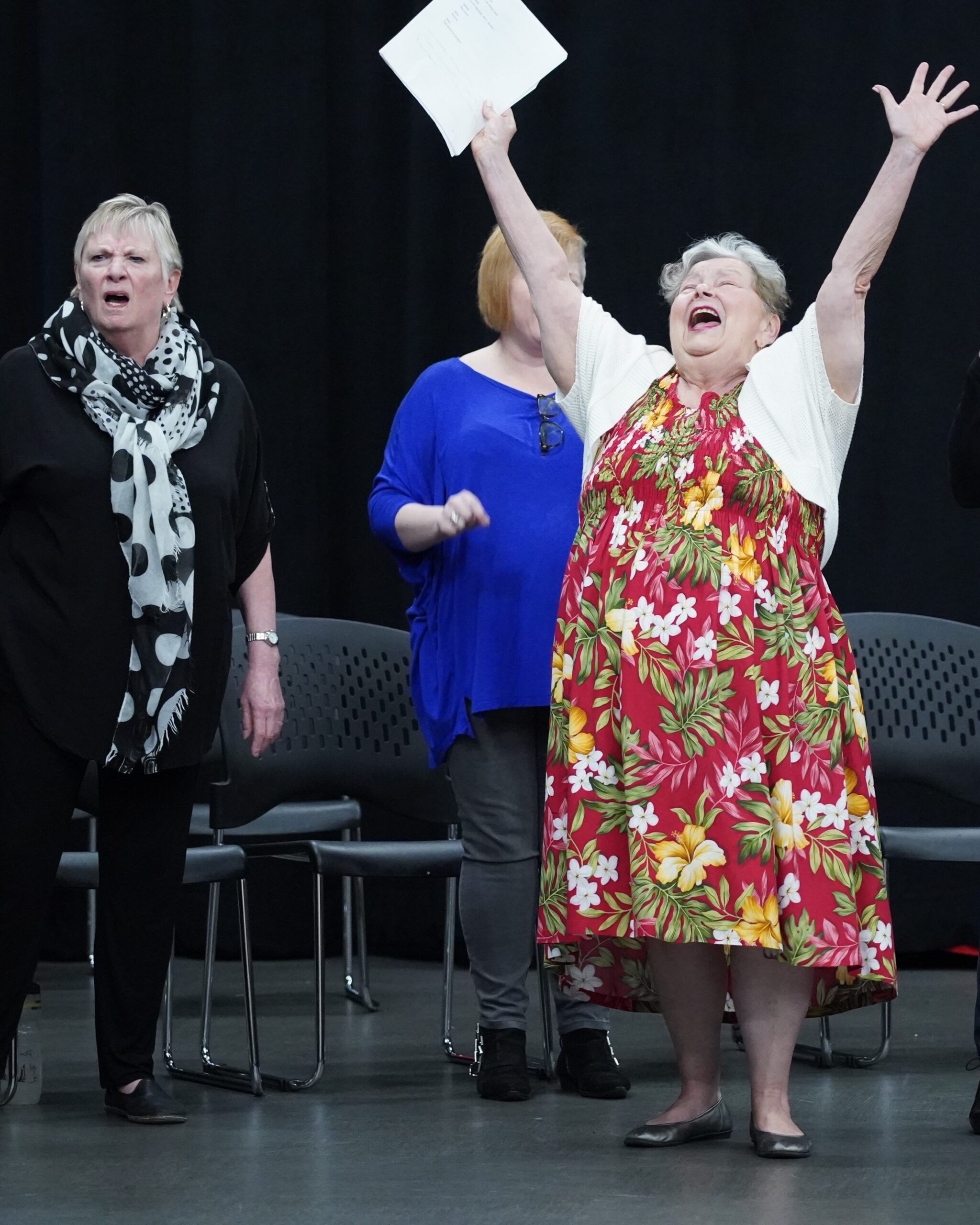 Bard for Life participants rehearsing. A woman on the left looks disgusted and a woman on the right looks elated with her hands raised in the air