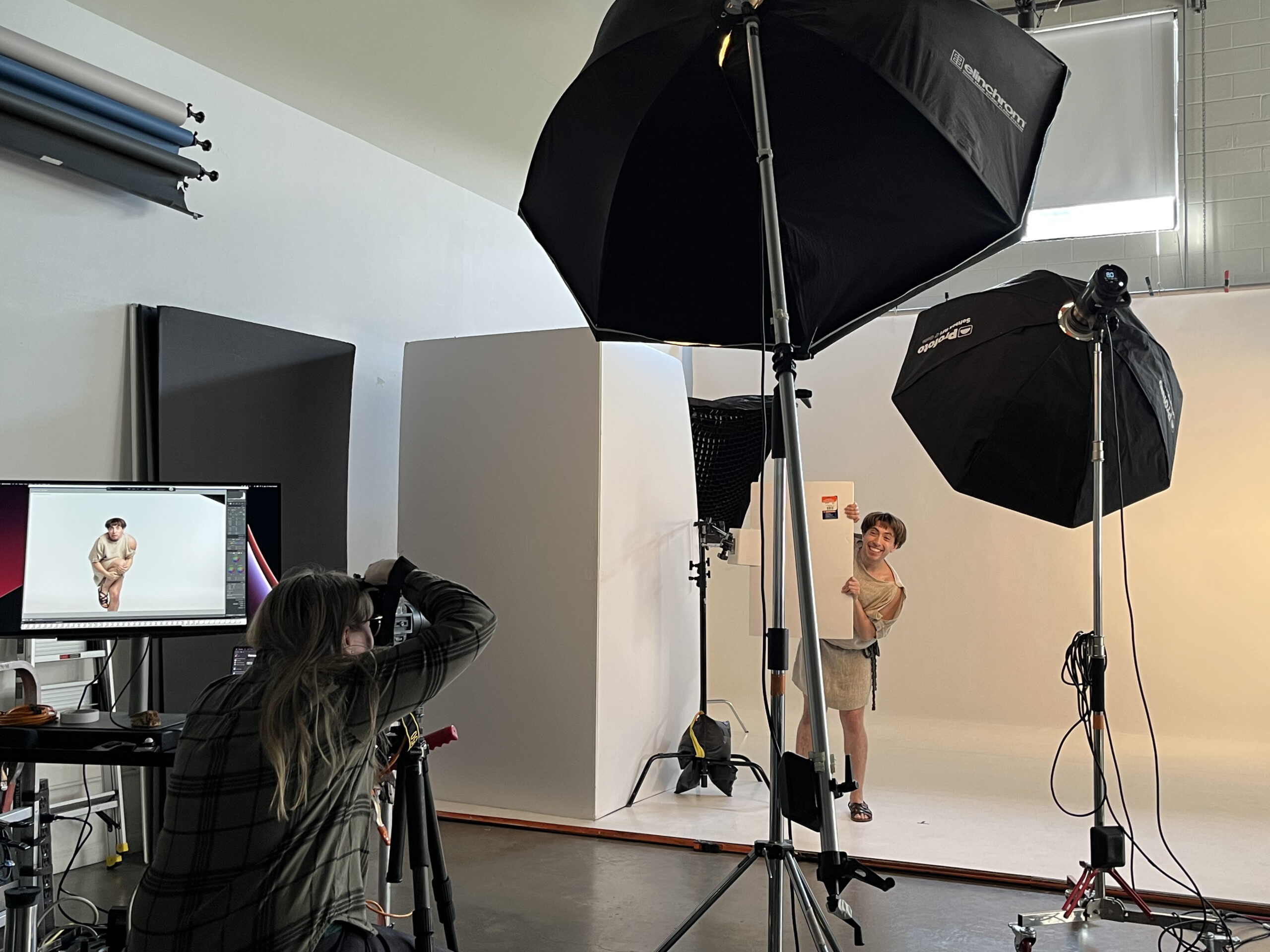 Tal, dressed as Dromio, peeks out from behind a makeshift wall at the photoshoot for The Comedy of Errors.