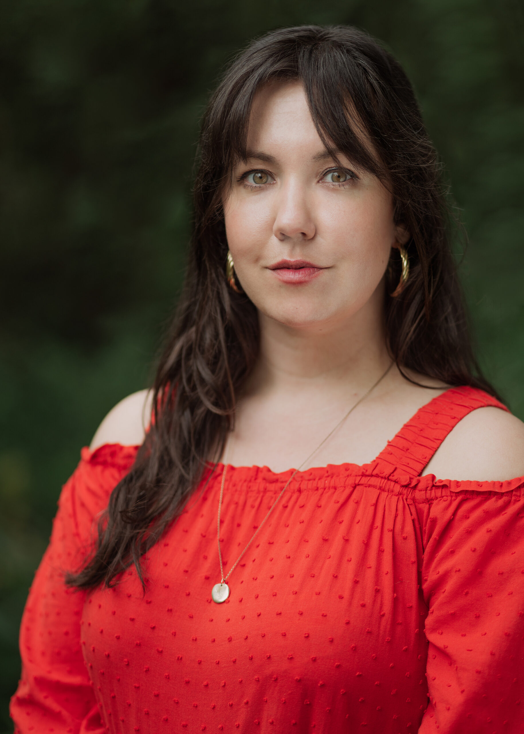 Christine Quintana looks into the camera. She wears a red cold-shoulder top.