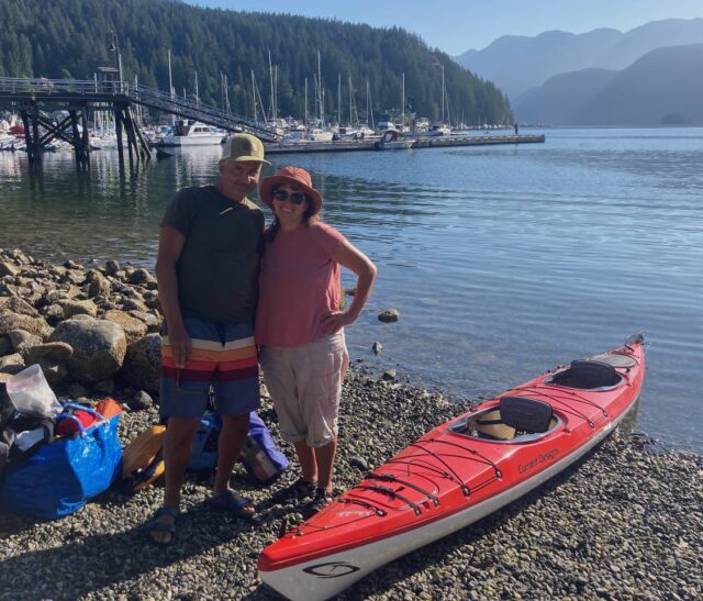 Marcus and his partner smile at the camera next to a two-person kayak.