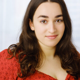 A headshot of Samantha Levy wearing a long-sleeve red shirt. She has white skin, long brown hair and brown eyes.