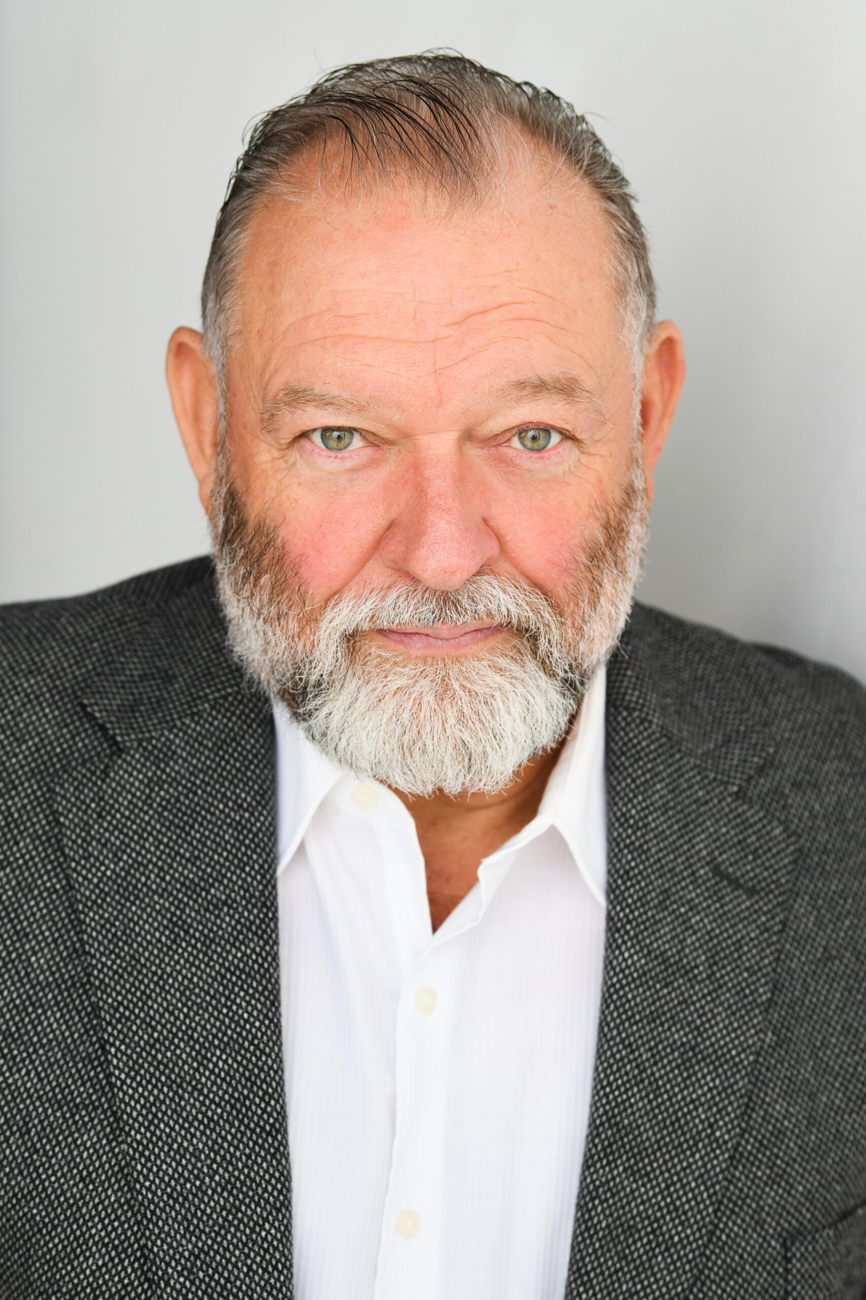 Dean Paul Gibson looks into the camera, wearing a grey suit jacket and whtie button-up.