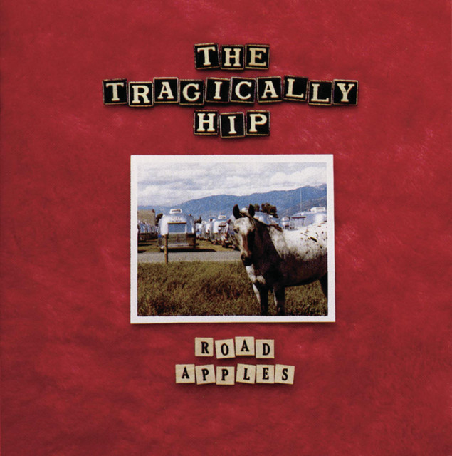 The Tragically Hip's album cover for "Road Apples" has a textured red background with a photograph of a horse, with an airstream and mountains in the background. The names of the band and the album are spelled out in wooden letter blocks above and below the photograph.