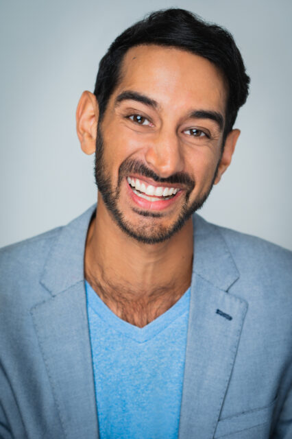 Chirag Naik smiles at the camera. He wears a blue blazer and V-neck t-shirt.