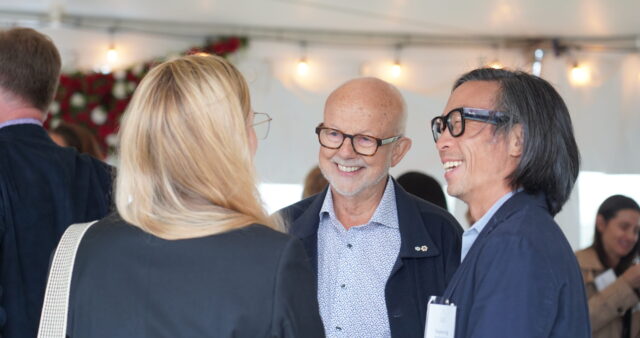 Christopher Gaze smiling while speaking with two people at a Member event